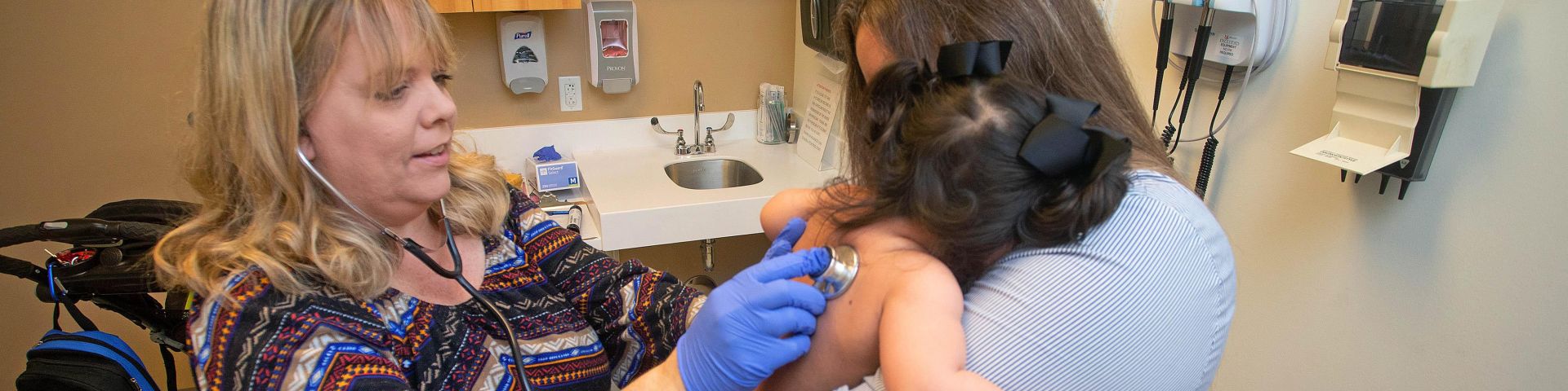 A provider from the Pediatric Complex Care Division examines a small child in their parent's arms.