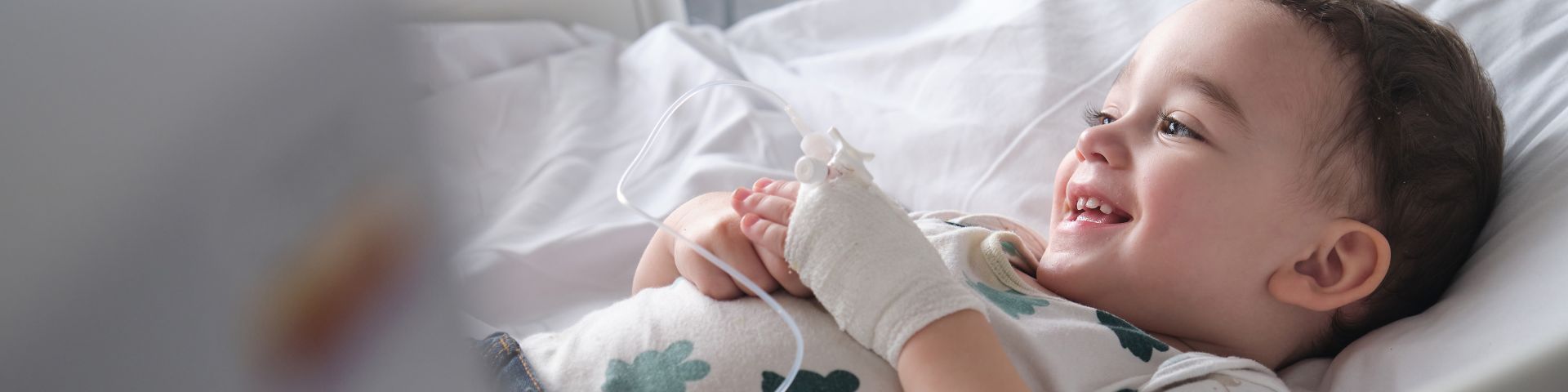 A child smiles while lying in a hospital bed.